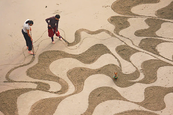 A tengerparton a homokba rajzol. Hogy mit? Messzebbről nézve lélegzetelállító